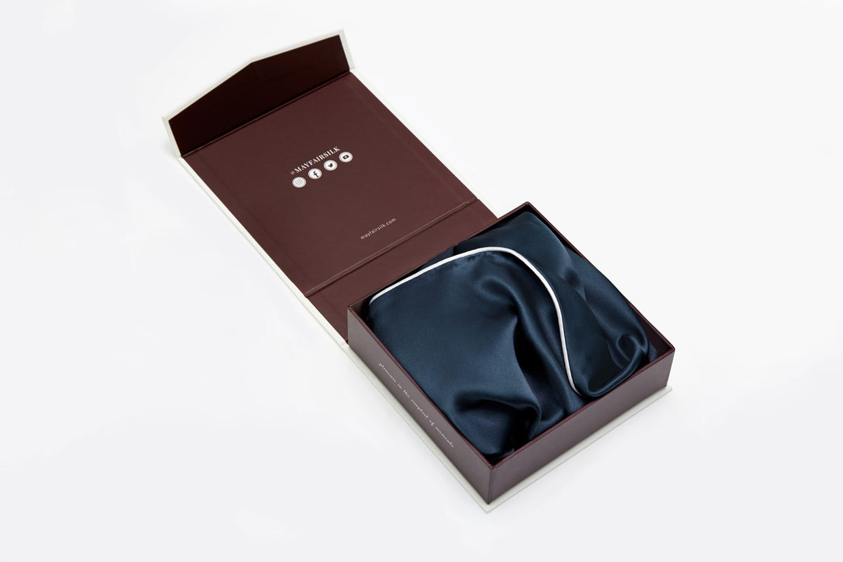 Midnight Blue silk pillowcase with ivory piping folded and displayed in a luxury gift box that is open