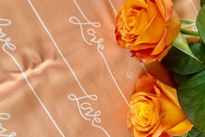 closeup shot of Love script on Peach Fuzz background with orange roses on right side