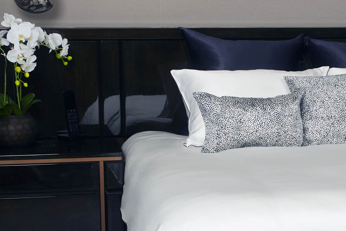 Luxury bedroom with black gloss bed with white silk bedding and pillowcases and leopard cushions in front and blue Euro shams in the back